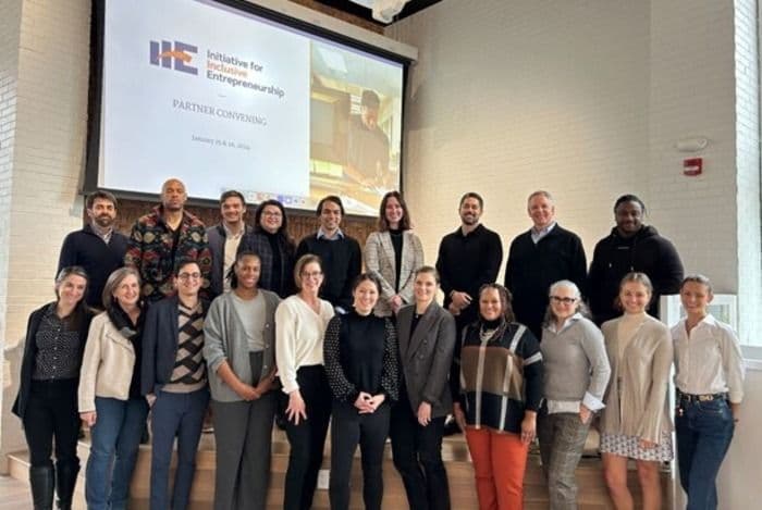 A diverse group of adults stands smiling in front of a projector screen displaying the IIE logo.