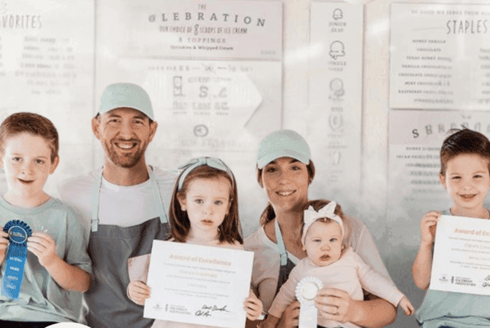 A proud family, two parents and four children, smiling in front of a shop menu.