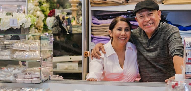 A smiling man and woman stand behind a counter in their small business.