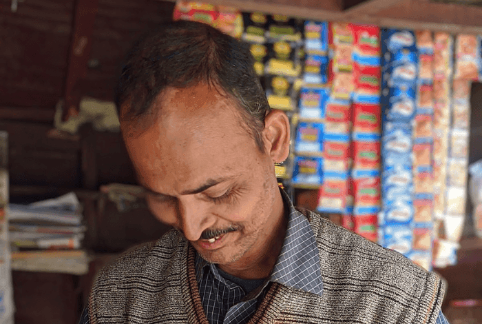 Man with a mustache wearing a vest, looking down in a shop with snacks.