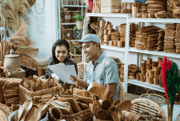Man and woman discussing documents in a bustling craft shop filled with wooden goods.