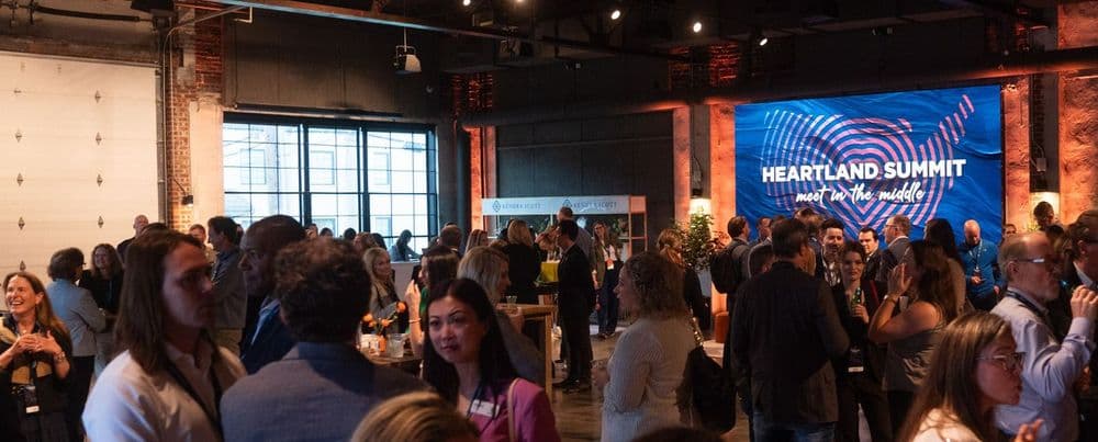 A large crowd at an event, with "Heartland Summit" displayed on a big screen.