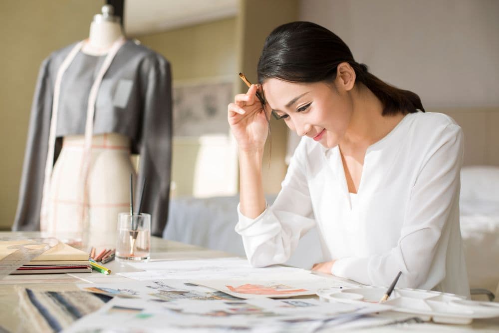 Woman designing clothes at a desk with a mannequin in the background.