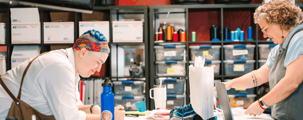 Two people collaborate diligently in a creative workshop with colorful threads and organized storage.