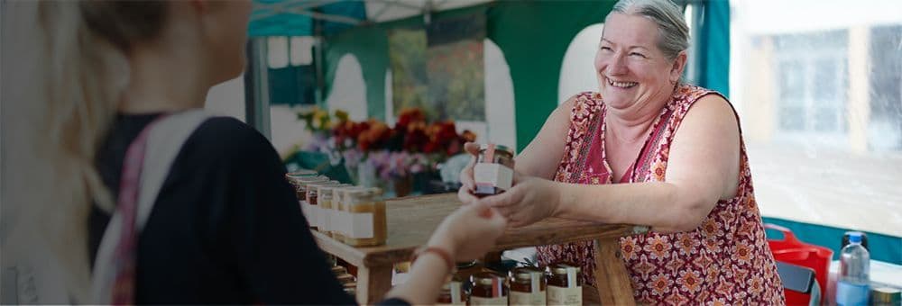 Smiling elderly woman in a floral top engaging with a customer at a shop.