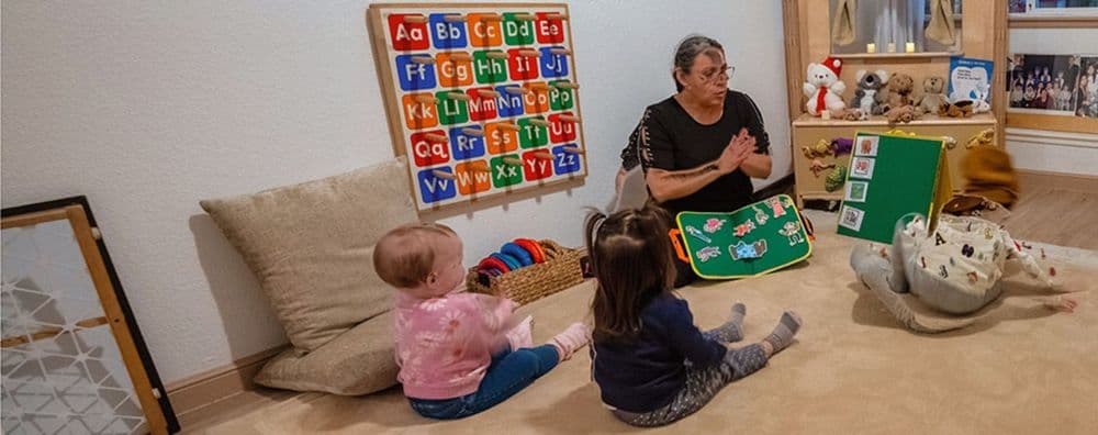 An adult reads a book to two toddlers sitting attentively on the floor indoors.