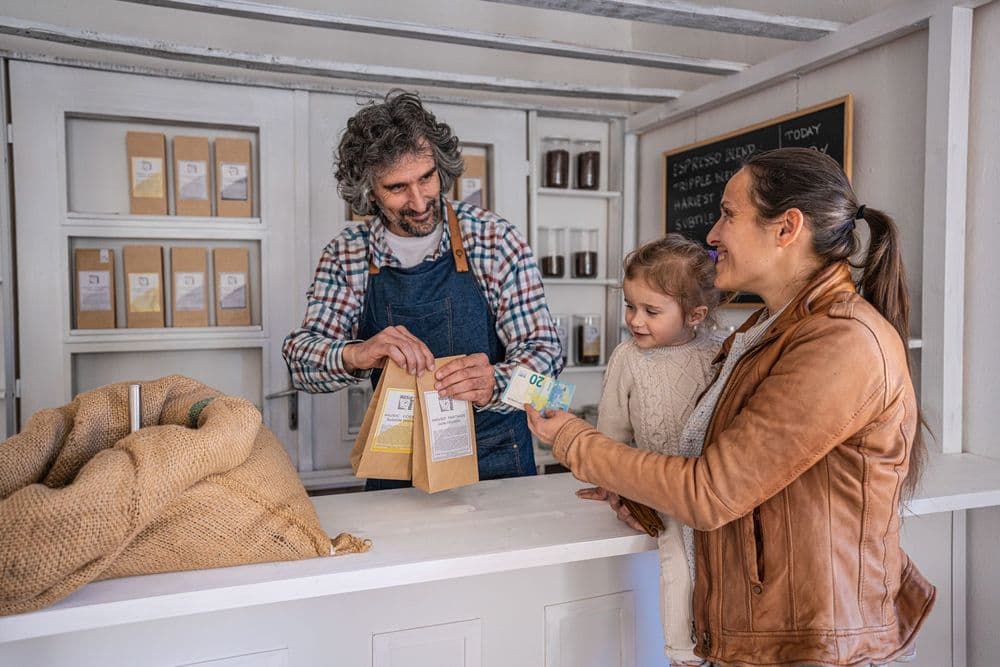 Store owner gives packaged goods to a smiling customer and her child.