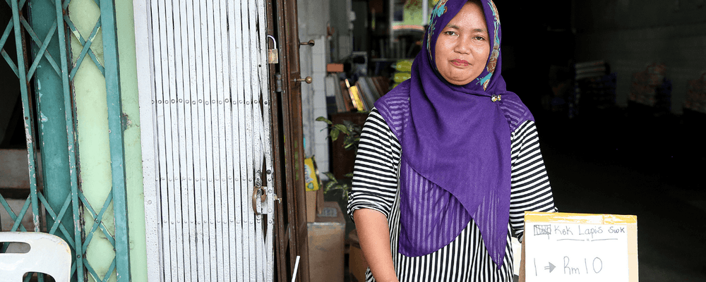 Woman in purple hijab smiles, holding a sign for 'R 10' outside a shop.