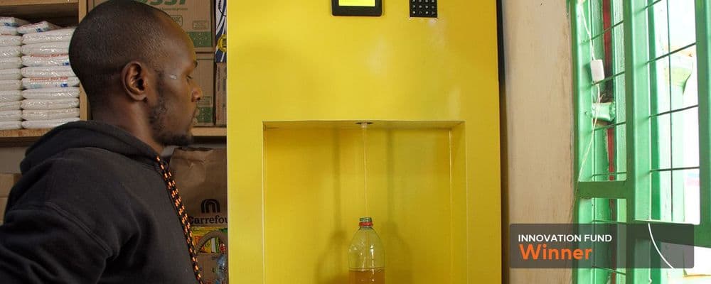 Man watches golden liquid filling a bottle from a yellow dispensing machine.