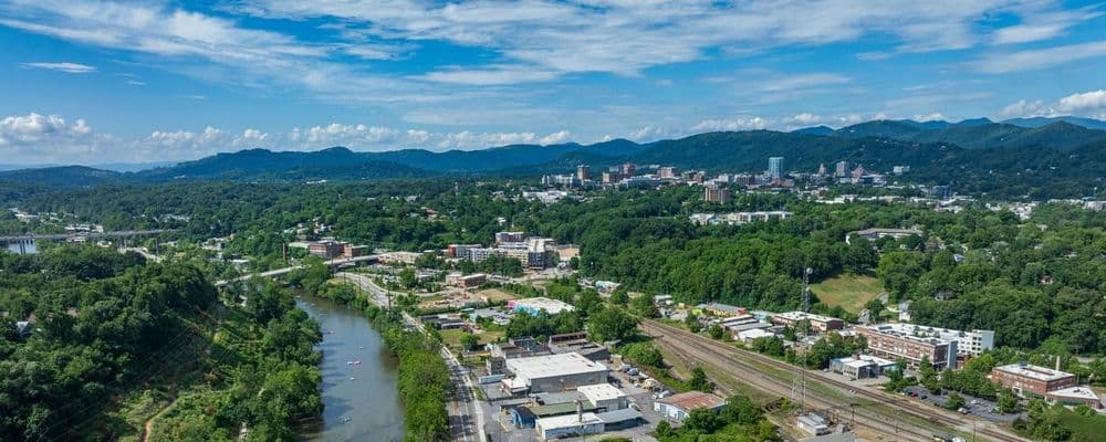 Aerial view of a river flowing past a city skyline with mountains in the background.