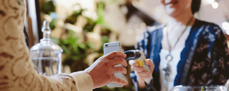 A customer holds their smartphone up to a scanner held by a shop assistant for payment.