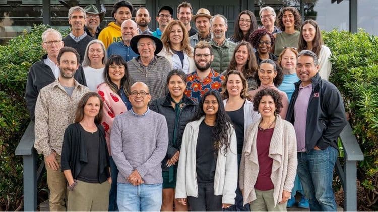 A diverse group of approximately thirty smiling individuals posing for a large outdoor group photo.