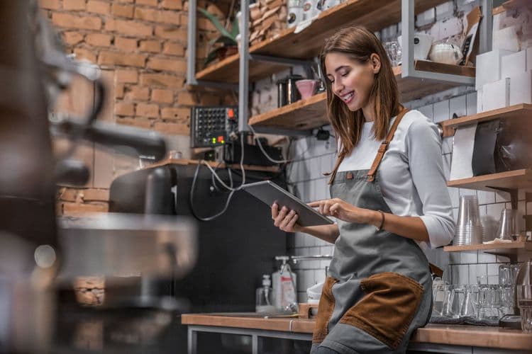Smiling barista using a tablet in a cozy coffee shop.
