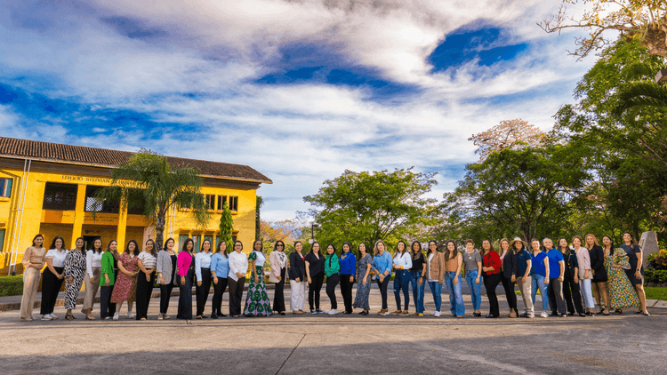 A large group of diverse professionals stands outside a yellow building under a bright sky.