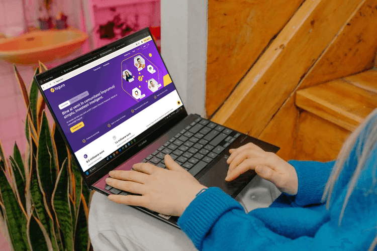Person typing on a laptop showing a purple website with illustrations of people.
