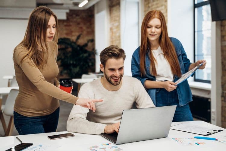 Three colleagues collaborate on a laptop, discussing a project in a modern office.