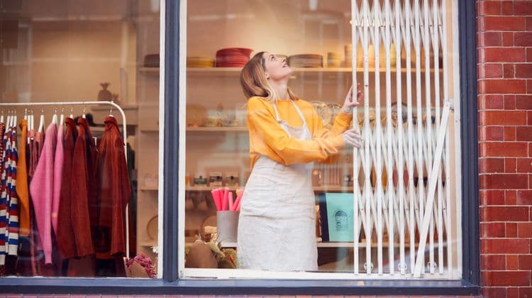 A woman in an apron looks up while operating a shop's security gate.