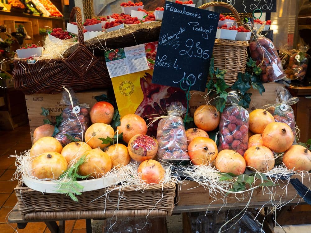 A colorful market stall displays fresh pomegranates, strawberries, and other produce in baskets.